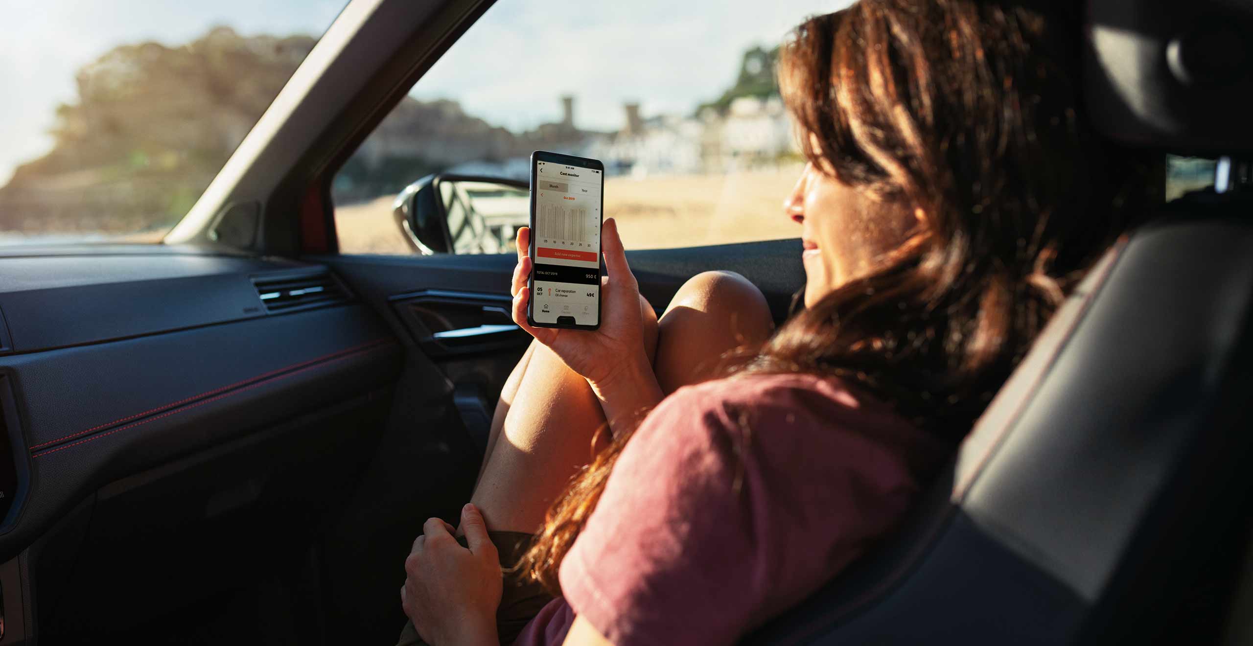 Woman seated in the passenger seat, browsing My SEAT App