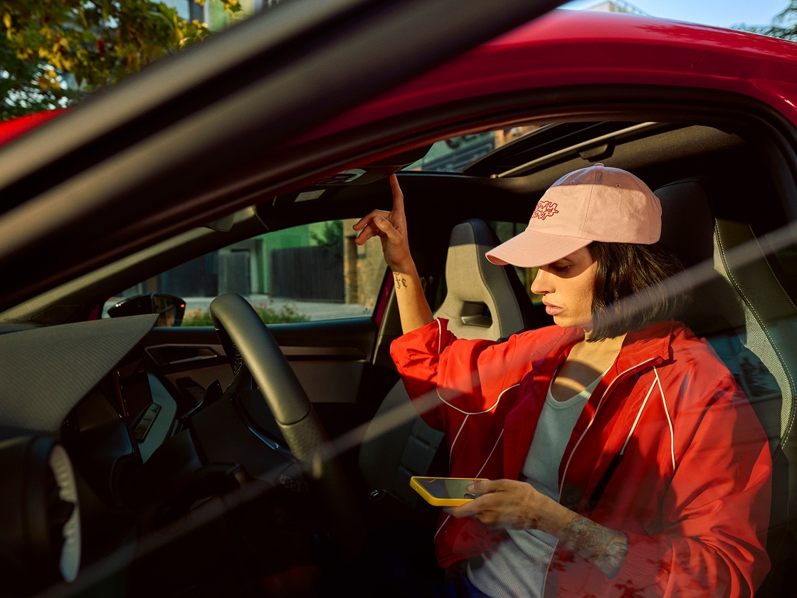 Person sitting inside SEAT Ibiza in red, holding a smartphone and interacting with the car interior 
