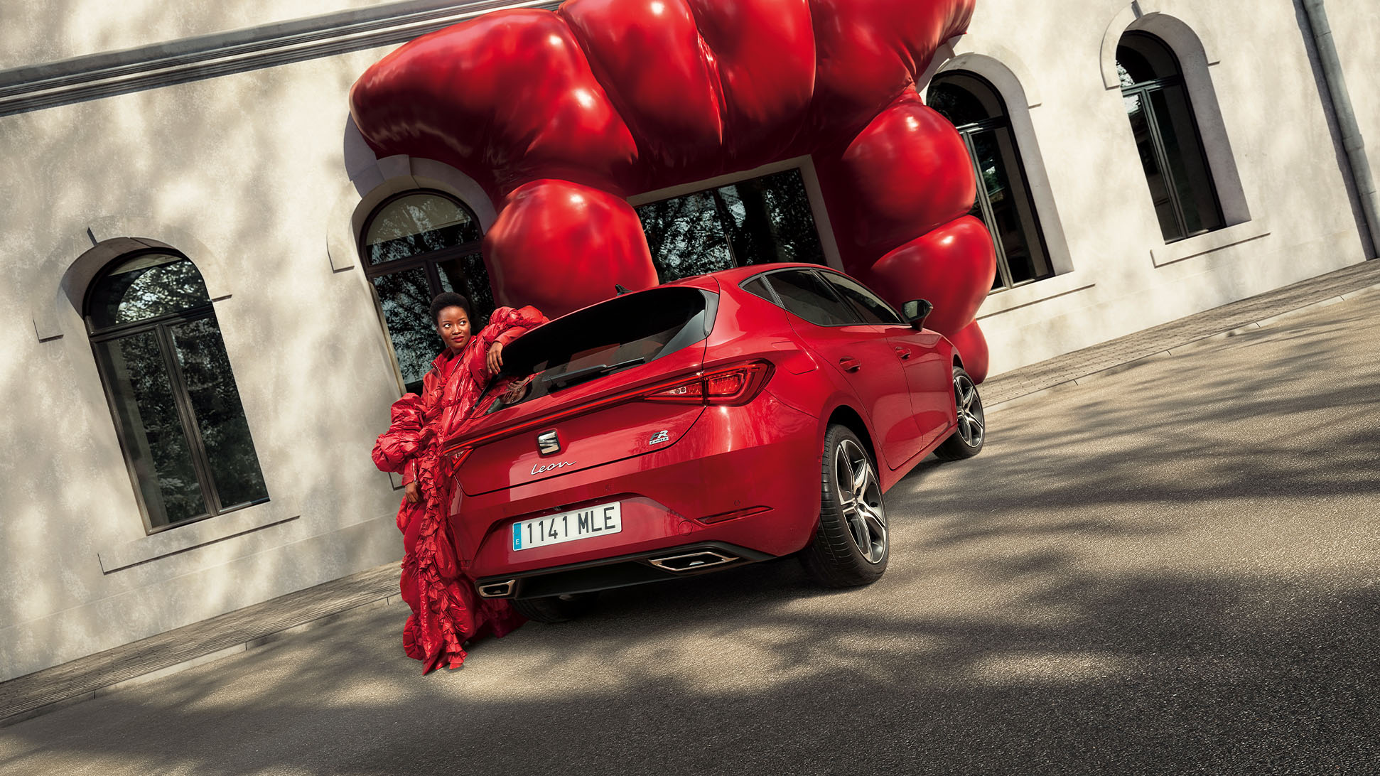 Woman lying on the back side of a plugged-in red SEAT Leon.
