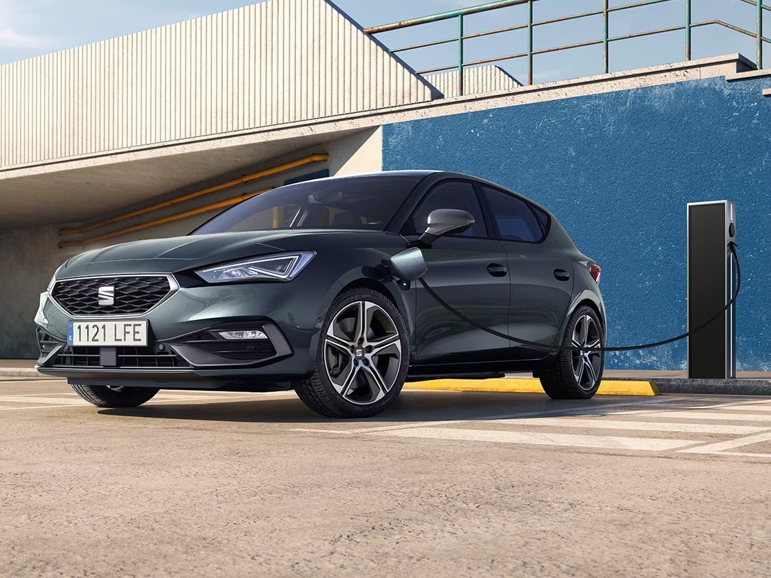 The seat leon e hybrid, a hybrid electric car, parked near a charging station, showcasing the e manager feature for impressive value.