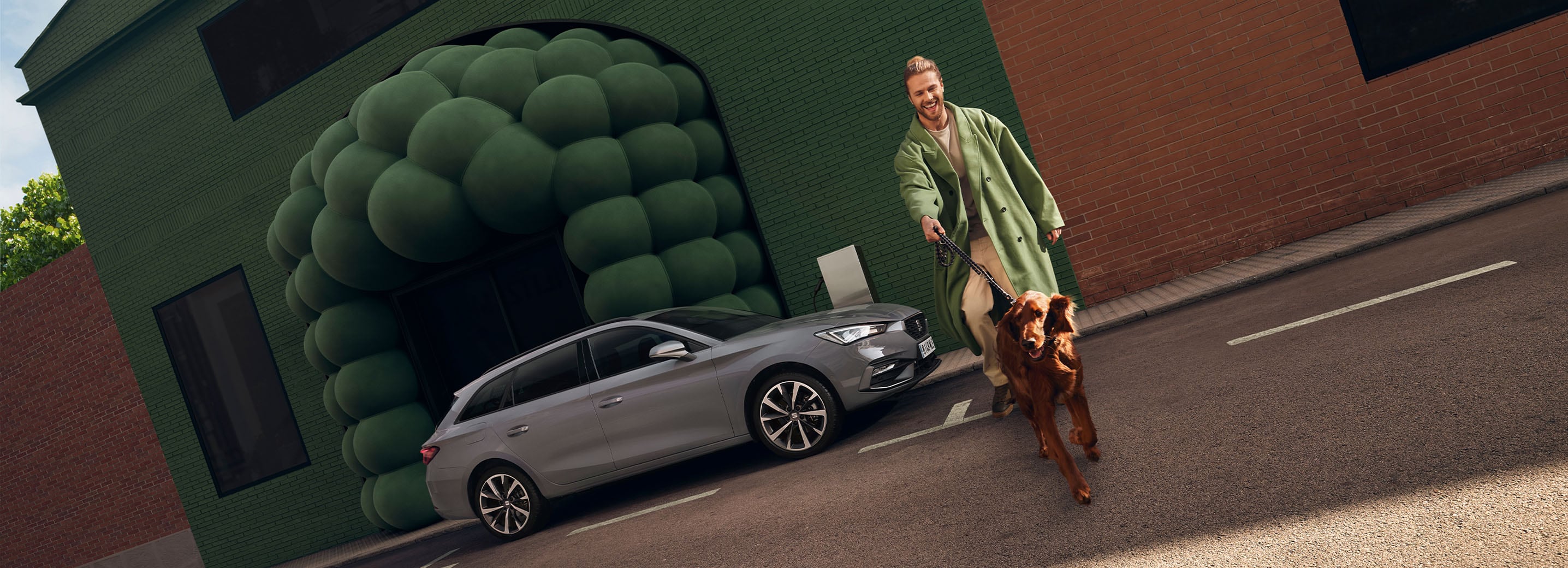 A grey seat Leon Estate and headlights with dynamic turn signals function. There is an individual walking nearby dressed in the same colours as the background.