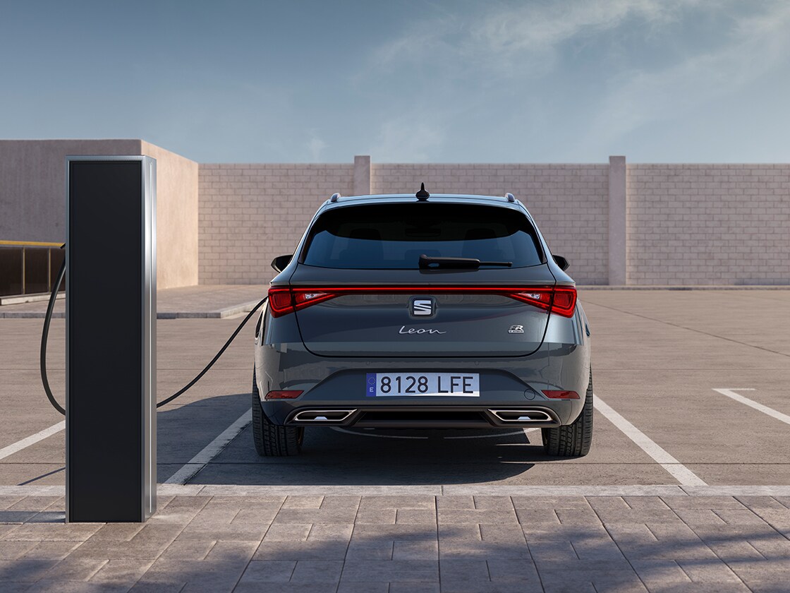 Rear view of the SEAT Leon Estate FR automatic car charging at a station, a new hatchback for 2025 in magnetic grey, complete with rear parking sensors and led headlights and taillights.
