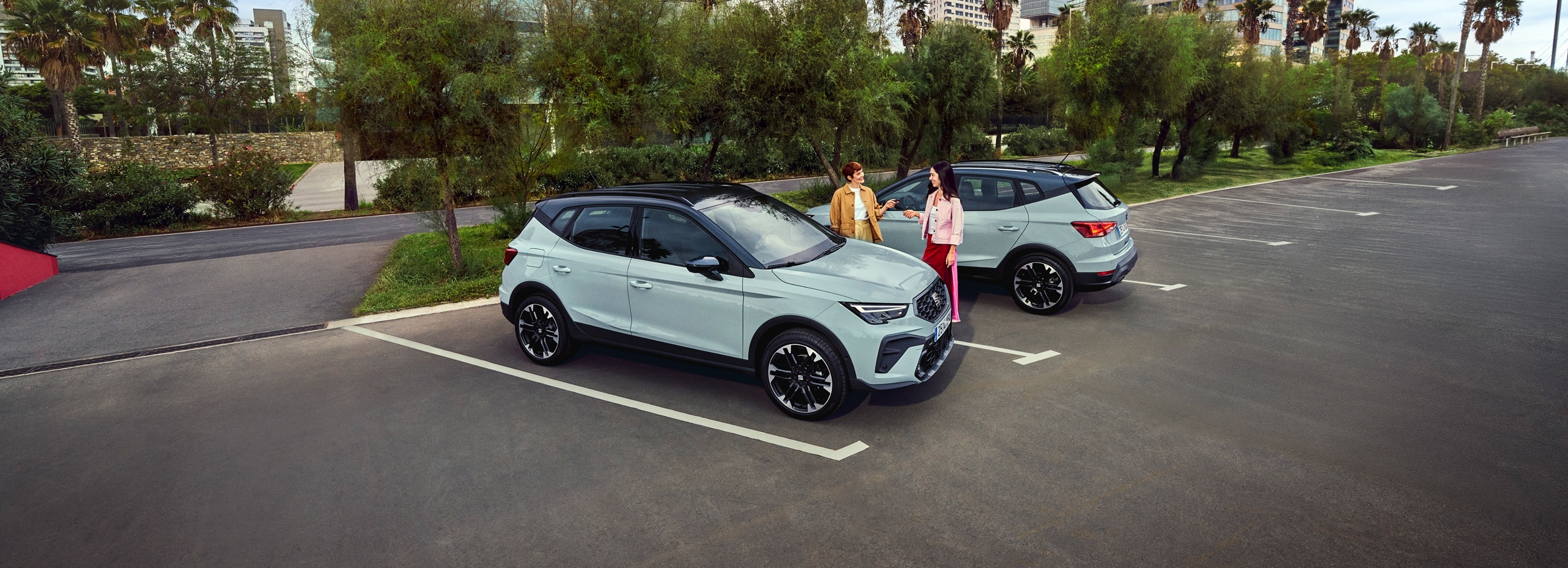 Two new SEAT Aronas in a car park with 2 people standing and talking in-between them