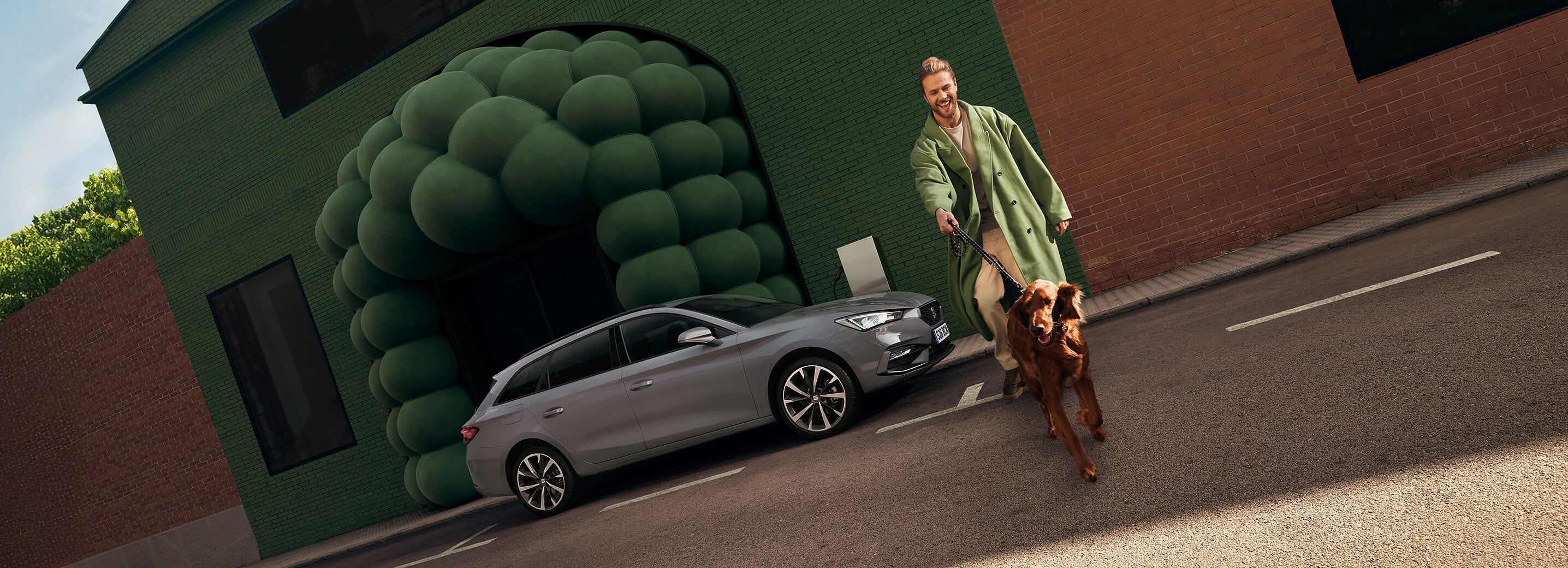 A man walking a dog in front of a parked SEAT Leon Estate