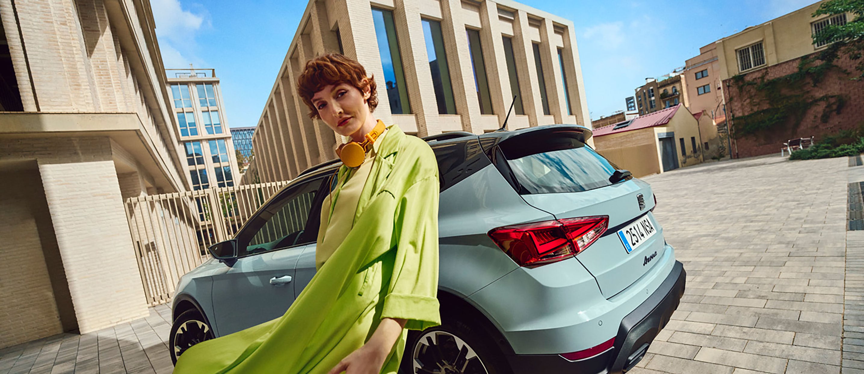 A woman wearing a lime green outfit with headphones with a SEAT Arona in the background