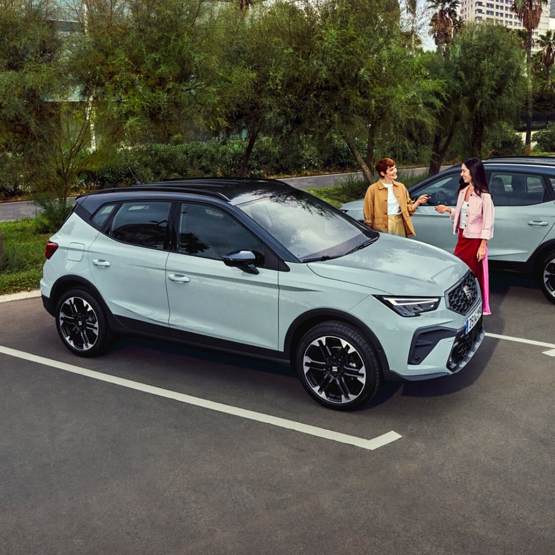 Two women standing next to a blue Arona in a car park