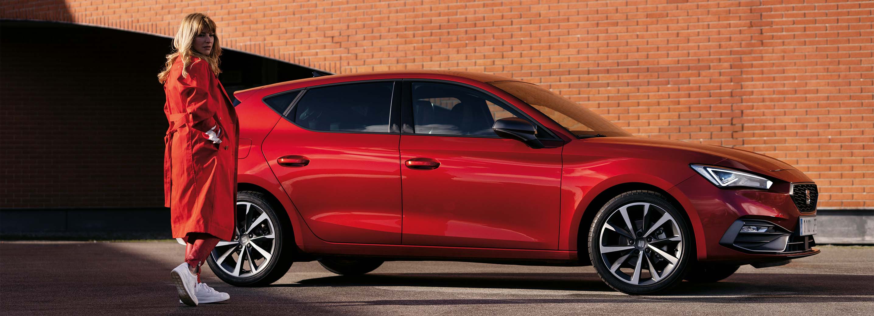 A woman dressed in red standing next to a red SEAT car