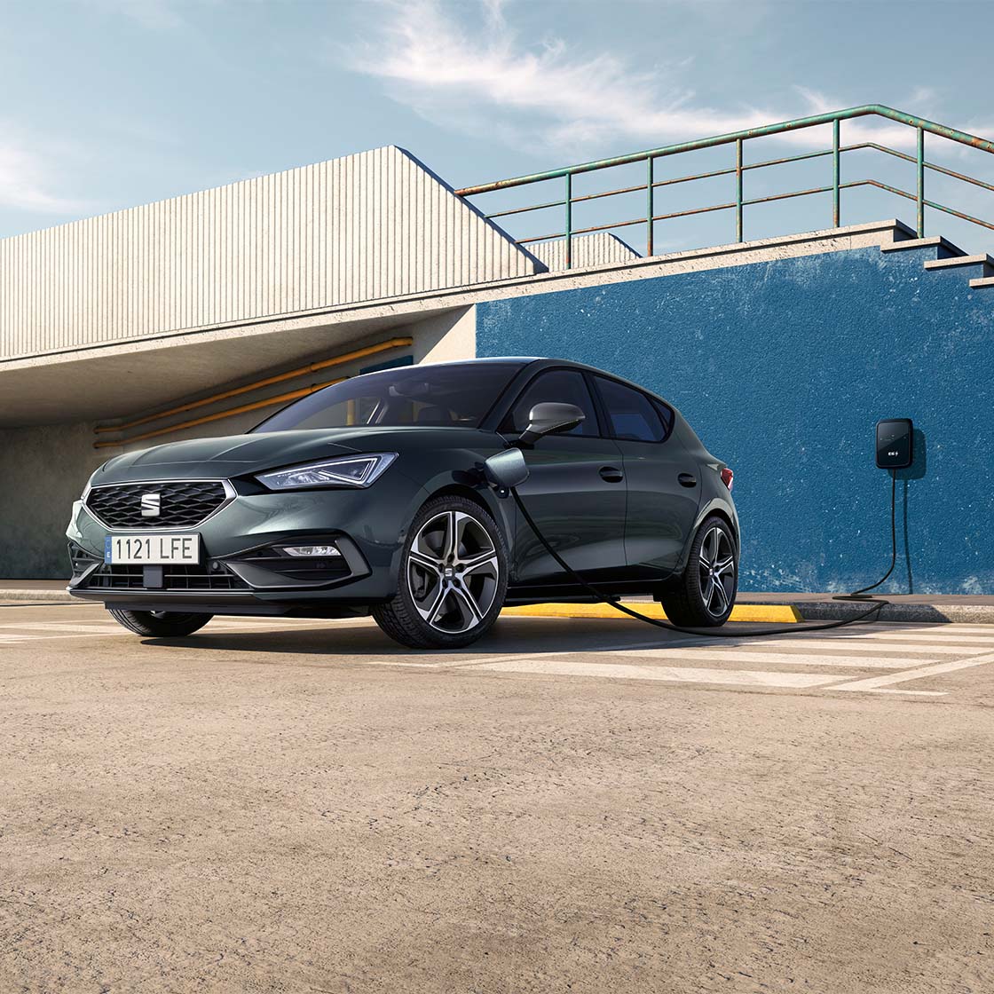 A plug-in hybrid SEAT Leon parked outside a building charging