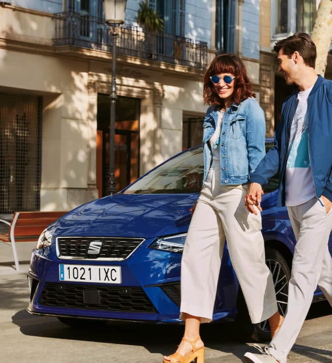 A couple walking next to a blue SEAT vehicle