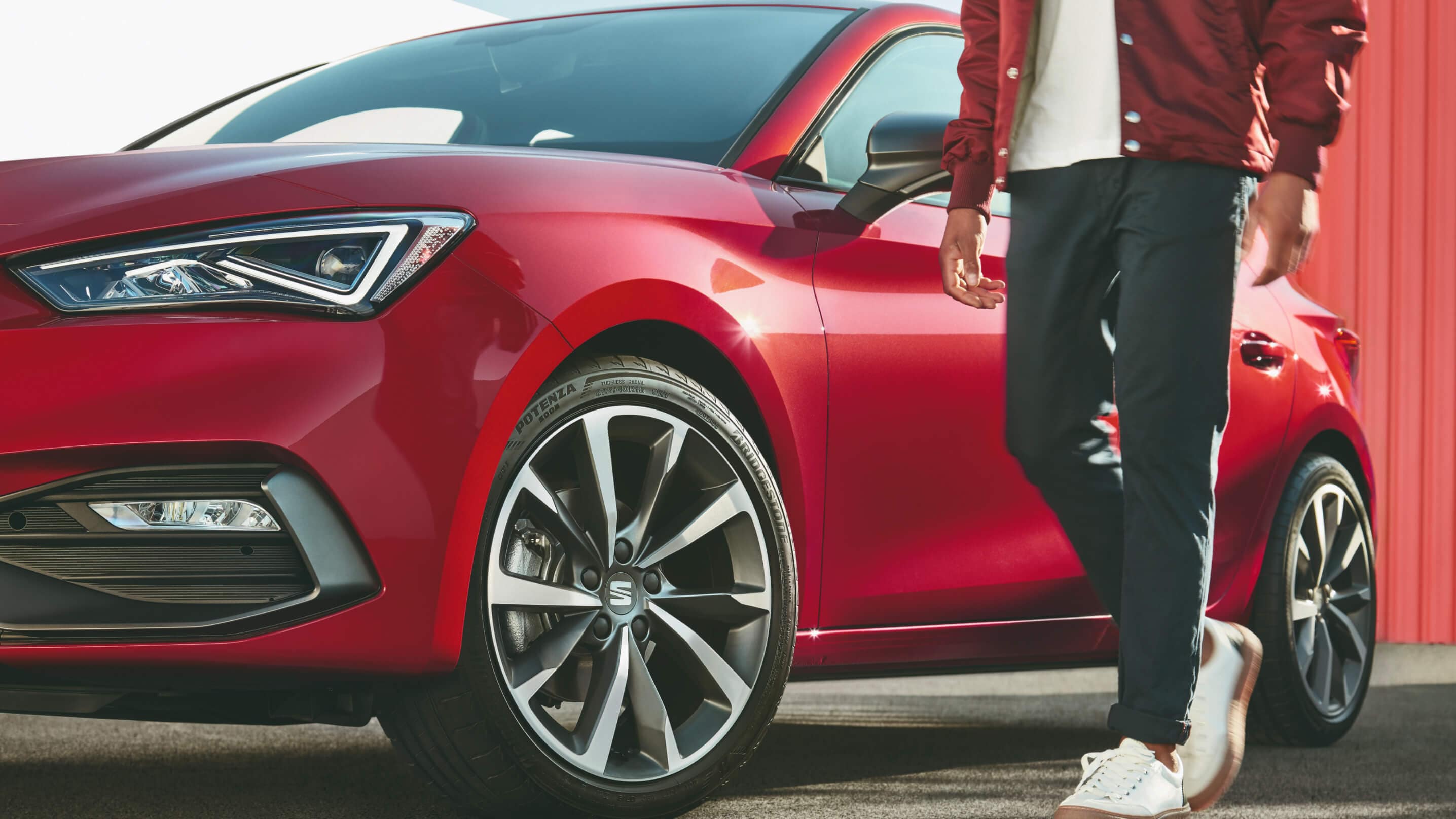 A casually dressed man standing next to a red SEAT Leon