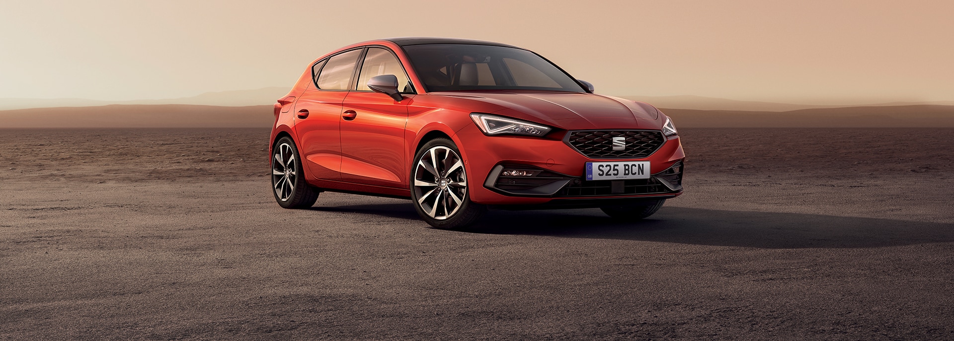 A red SEAT Leon parked in a sandy landscape with dunes in the background
