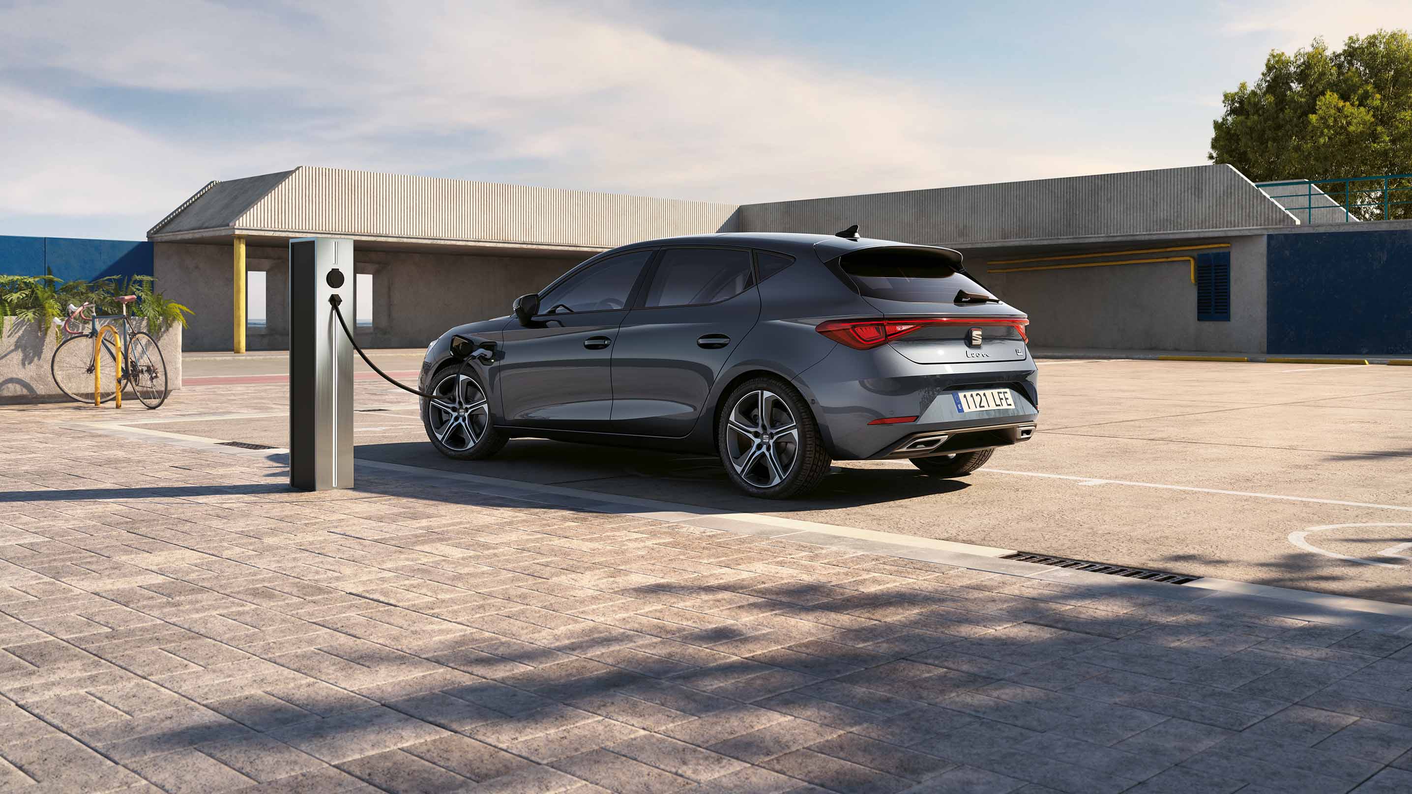 Rear view of a SEAT Leon plug-in hybrid charging by an industrial looking garage
