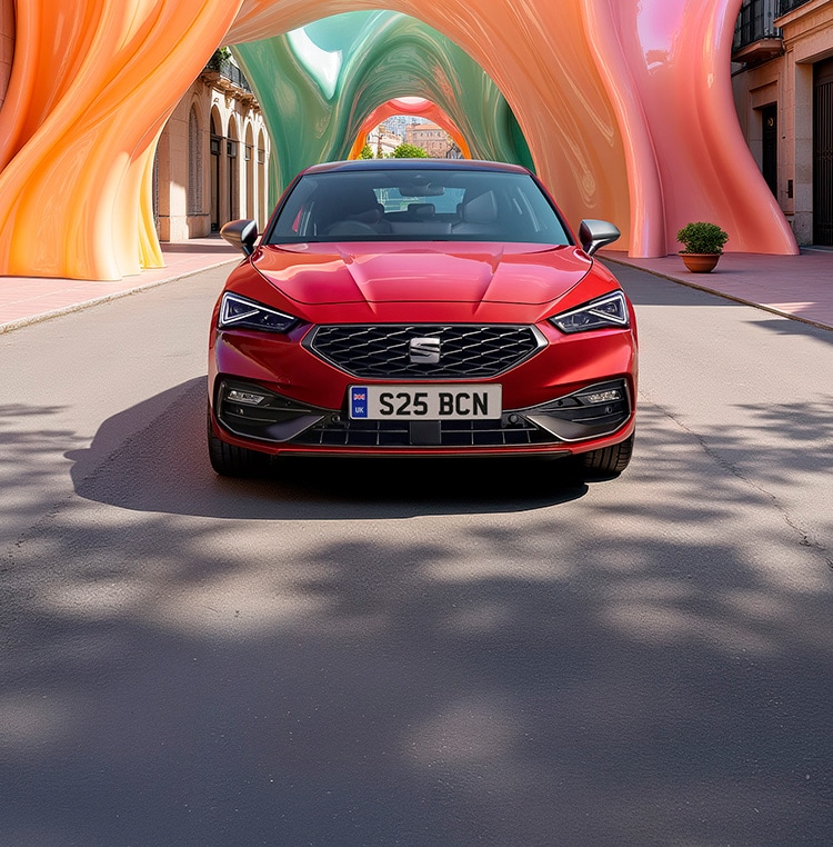 Front facing SEAT Leon in red with a colourful yellow, orange and pink arch in the background