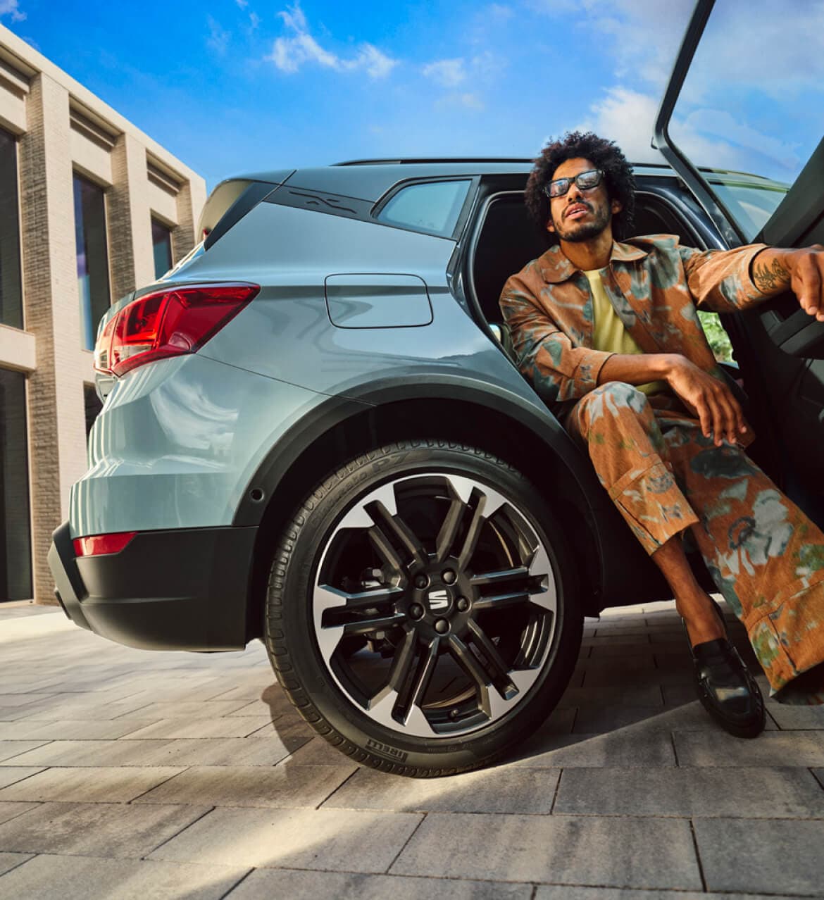 a man wearing sunglasses sitting into the back of a light grey SEAT car