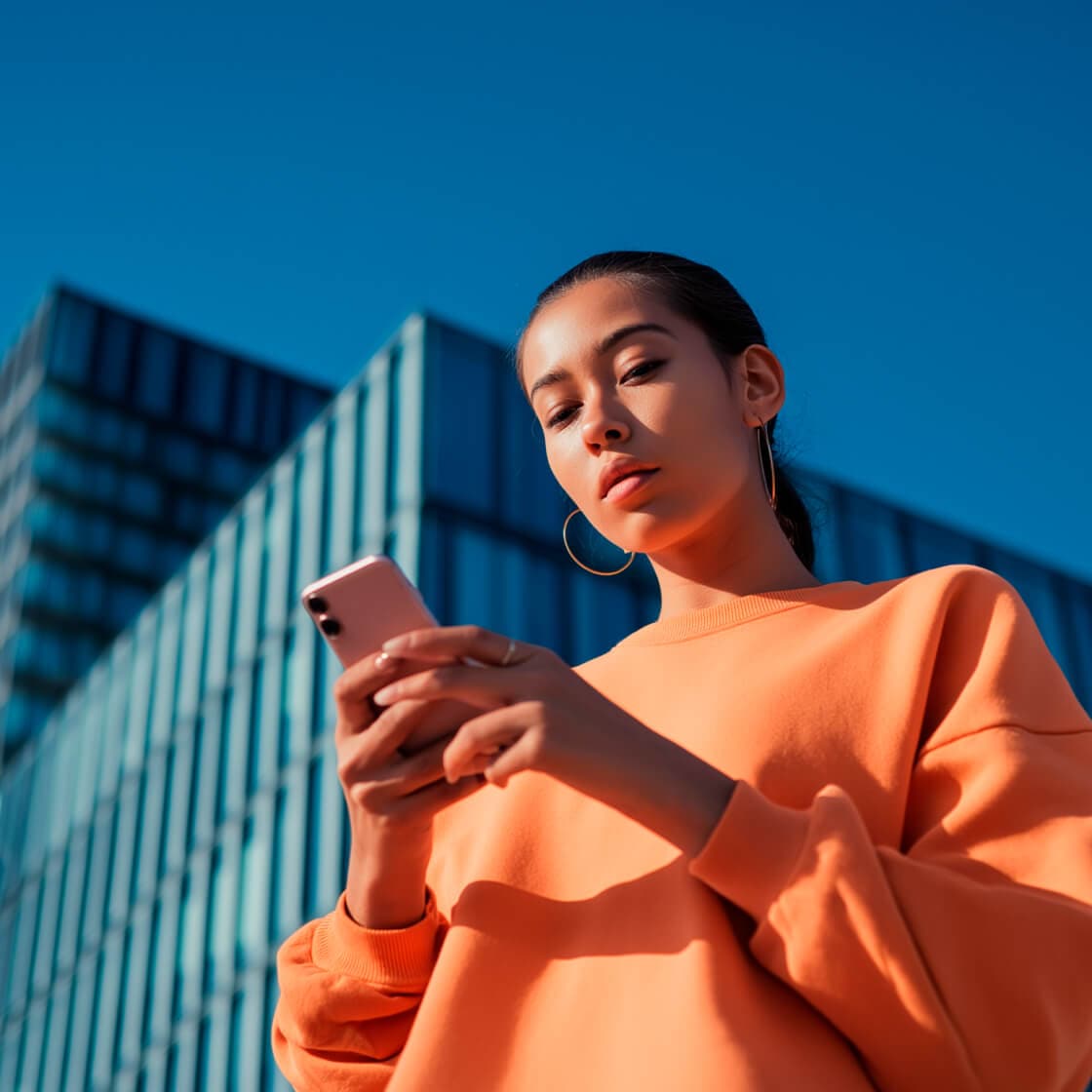 low angle of a woman in an orange jumper looking at her phone