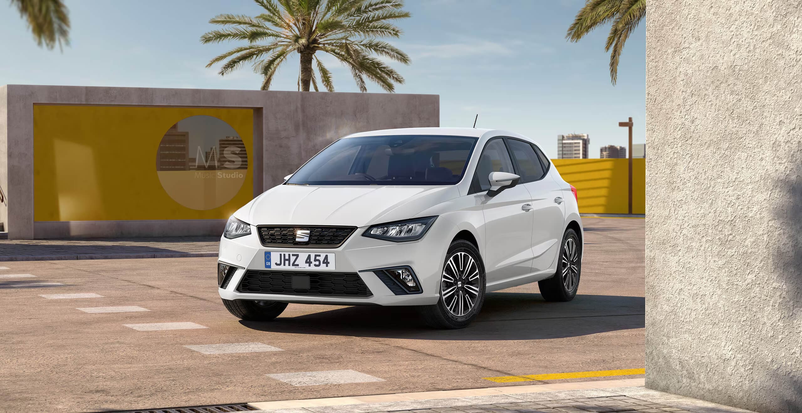 A white SEAT Ibiza SE Technology parked next to a building with tropical trees in the background
