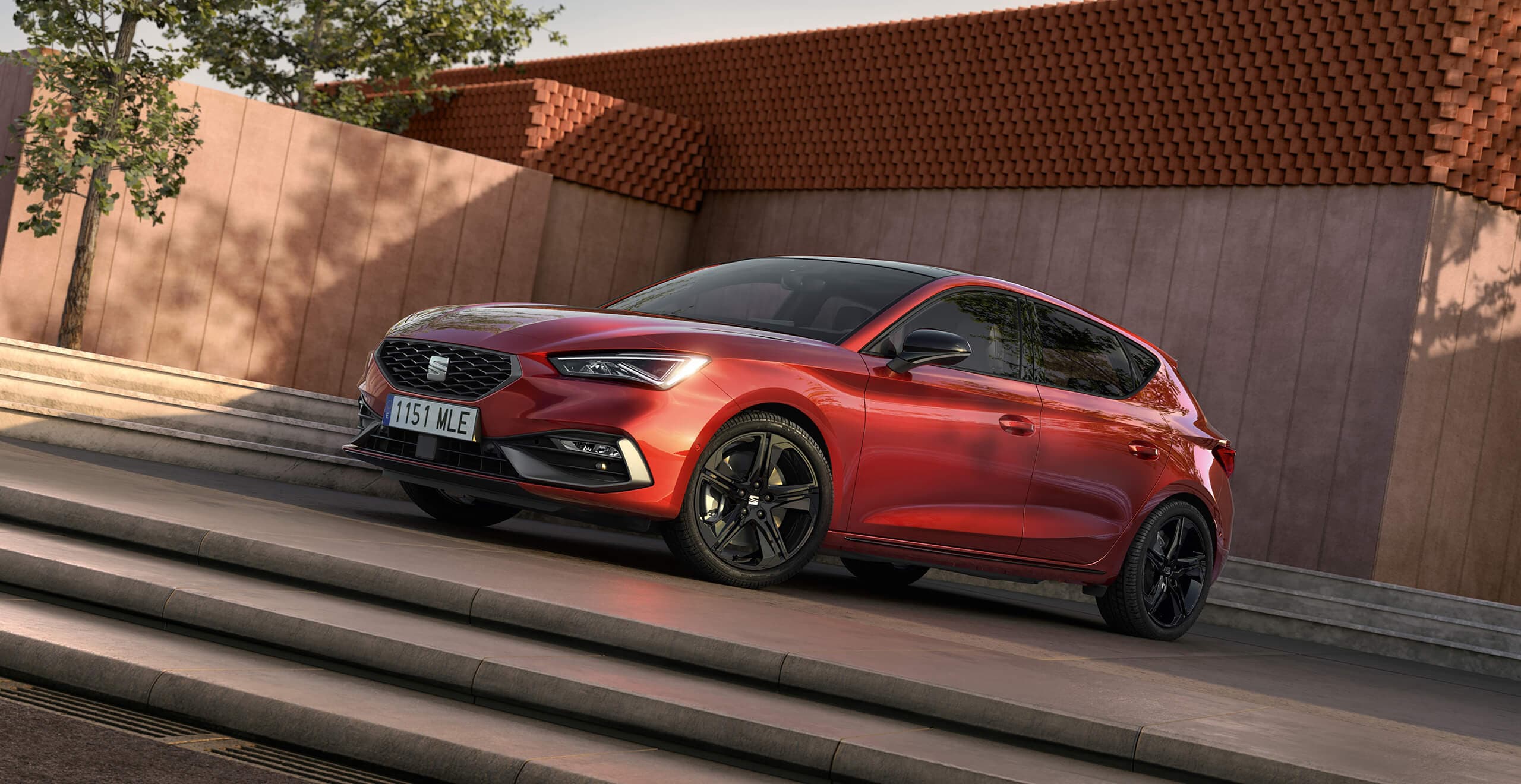 A white SEAT Leon parked with a red wall in the background