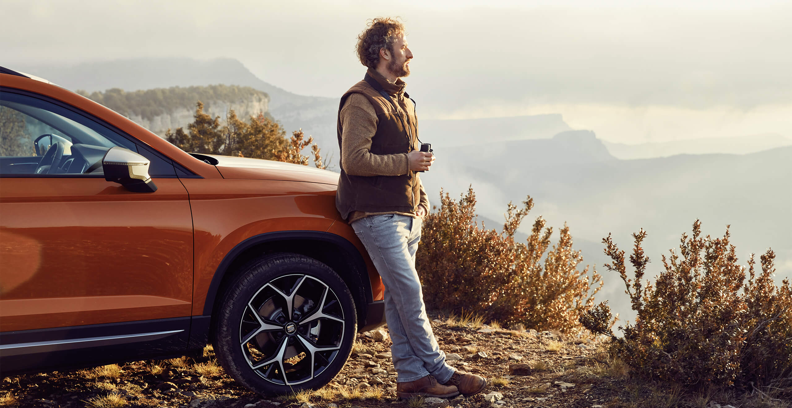 Man stood against a SEAT Ateca looking at mountainous view