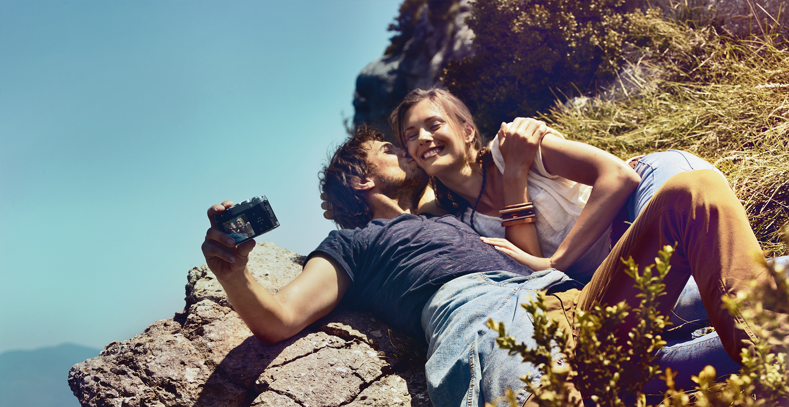 Young couple lying on a hill taking a selfie in sunshine – SEAT Used car warranty deals