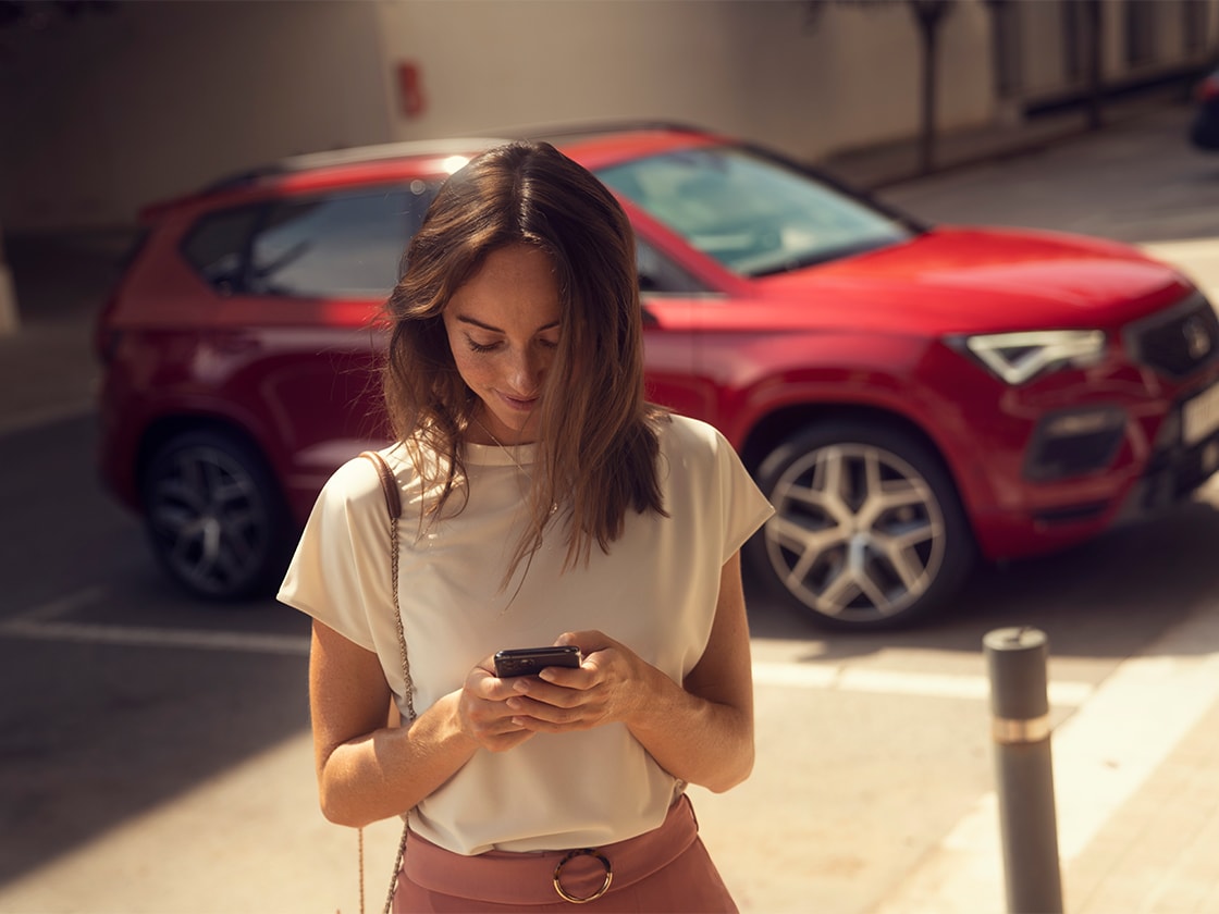 A woman with smartphone standing in next to a red SEAT Ateca