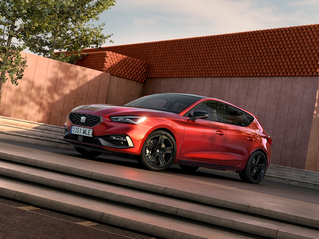 Two people standing next to a red seat leon in a sunny location with palm trees, highlighting the benefits of seat’s extended warranty.