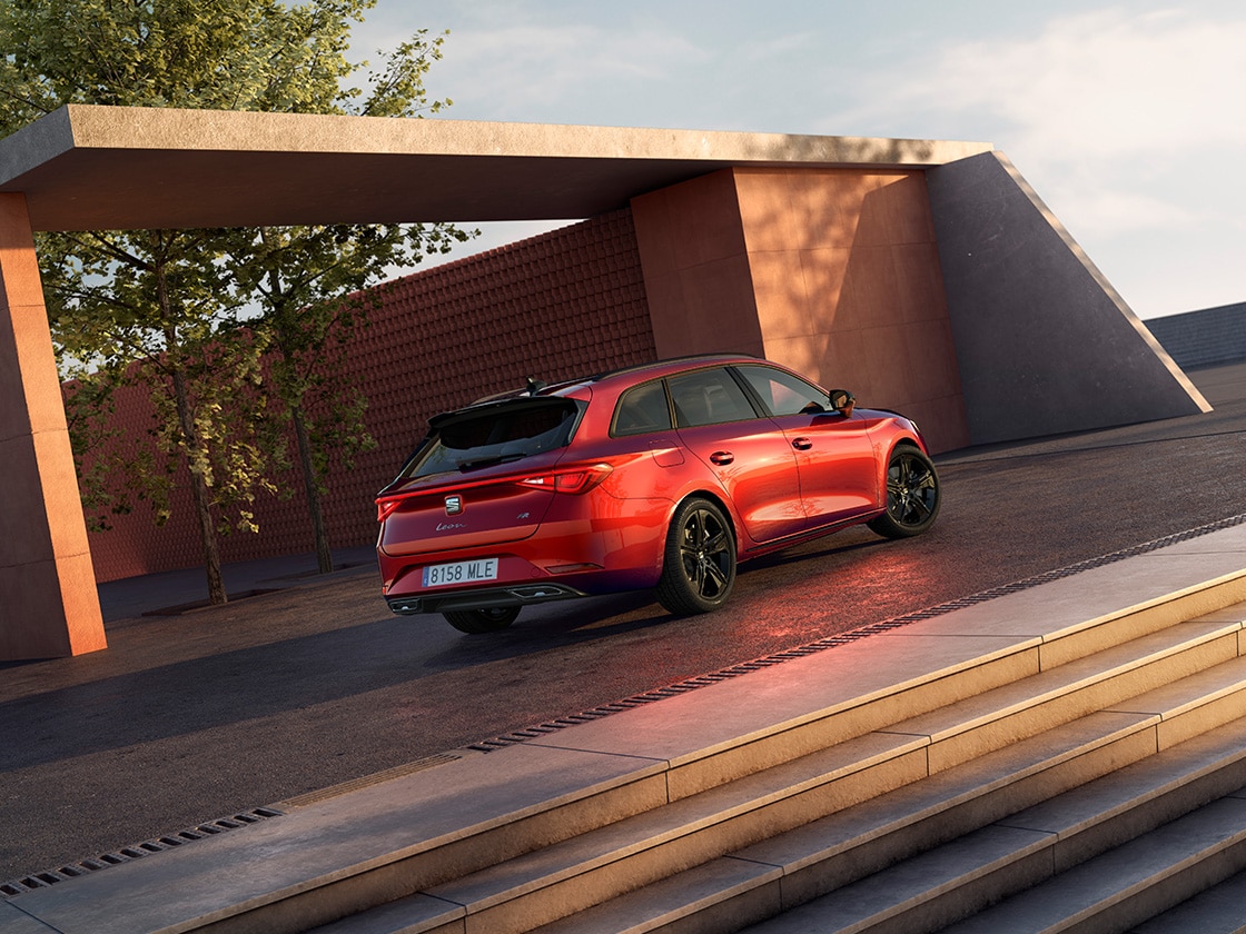 Glossy black mirror covers for the SEAT Leon Estate FR contrasting with the red car body, side view with cement background.
