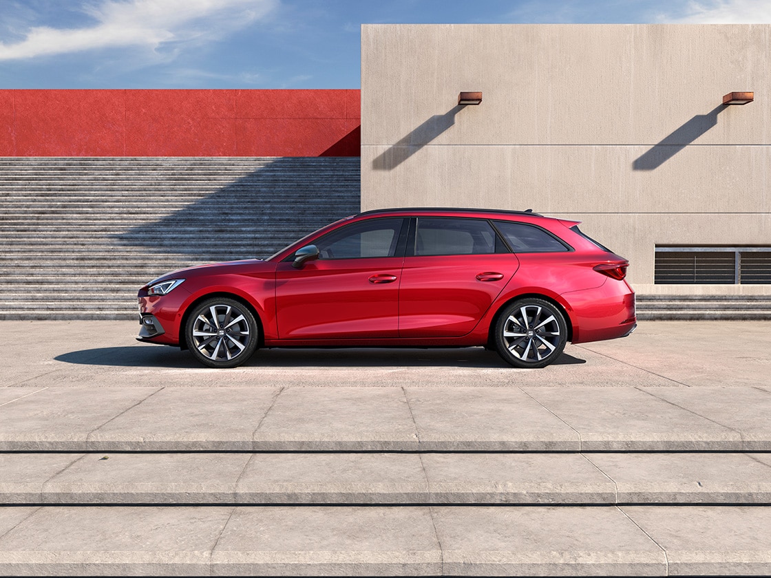 A red SEAT car parked inside a dark parking space where there is a glimpse of sun facing the car and the individual standing by the car.
