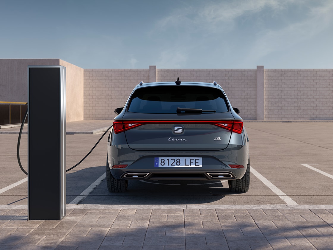 Rear view of the SEAT Leon Estate FR automatic car charging at a station, a new hatchback for 2025 in magnetic grey, complete with rear parking sensors and led headlights and taillights.