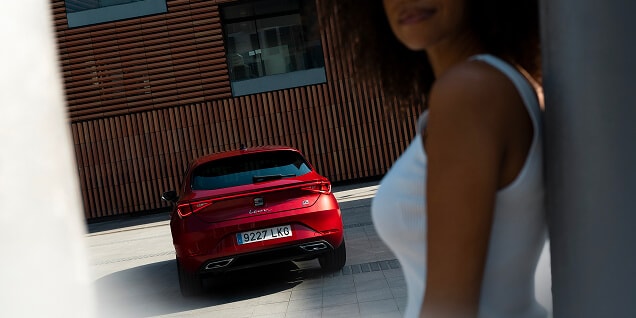rear view of a red leon 5d,parked in an open parking space and a woman, as main object of the photo, leaning on a pole