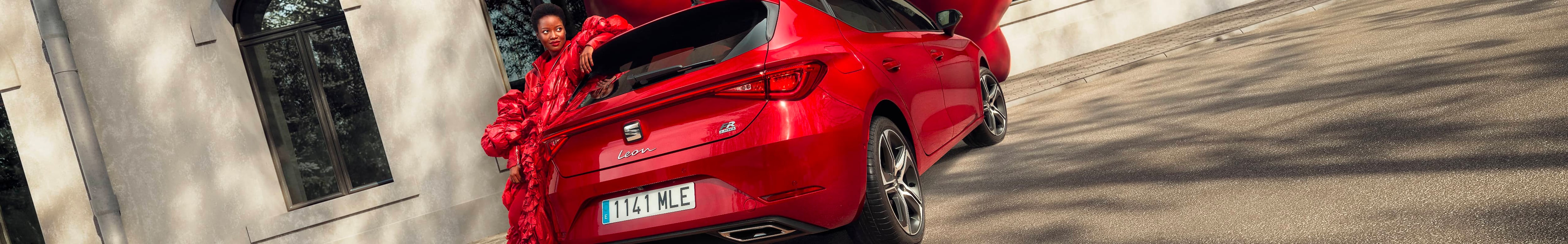 rear view of a red leon 5d,parked in front of an old building and a woman dressed in red, leaning on the back of the car