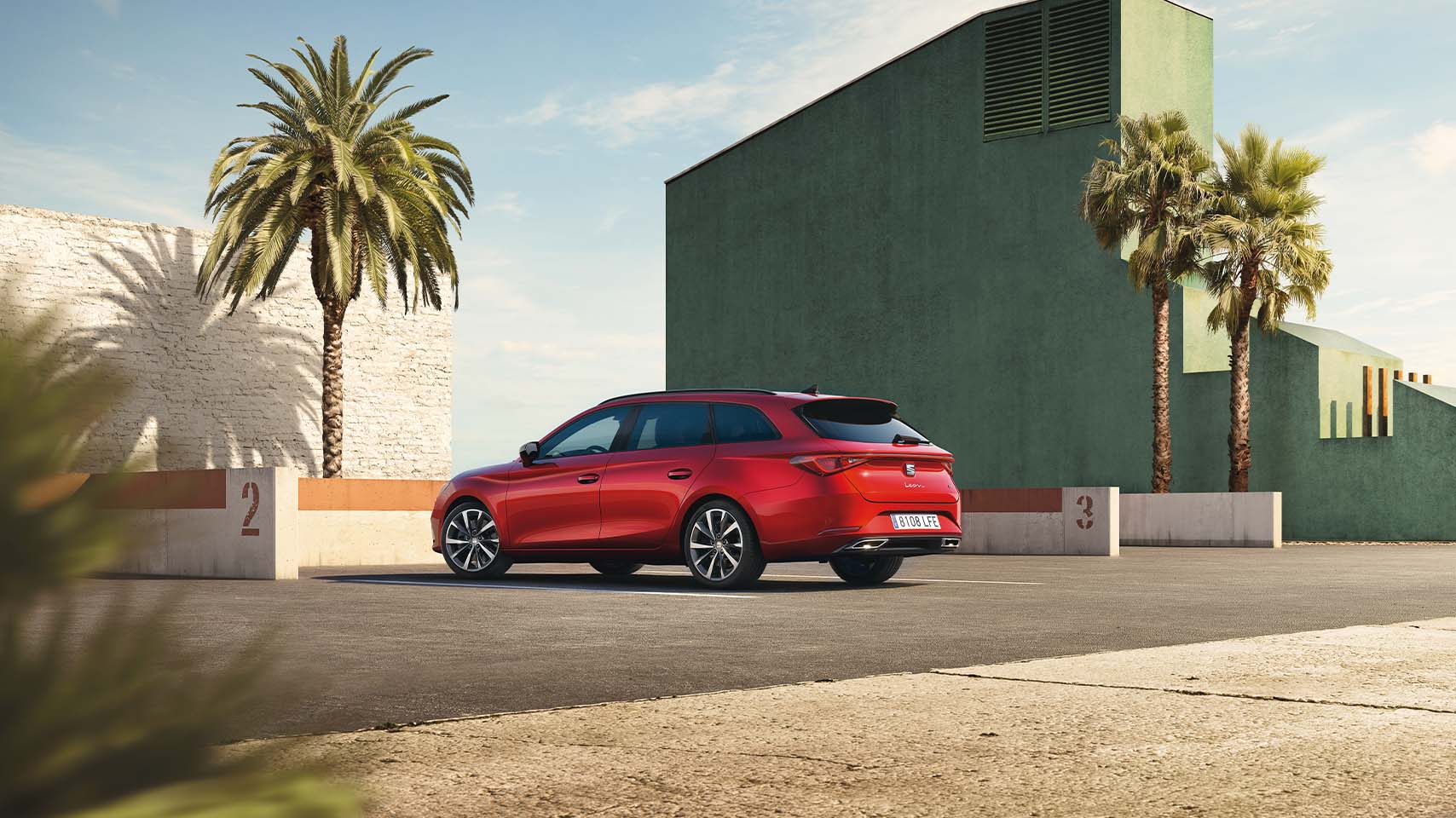 Mild hybrid electric vehicle, SEAT Leon in red, three quarter rear view and green building